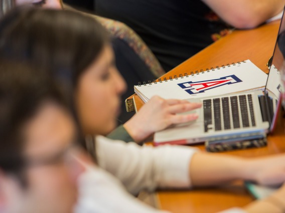 students at desks, one with a notebook with the Arizona logo prominently displayed
